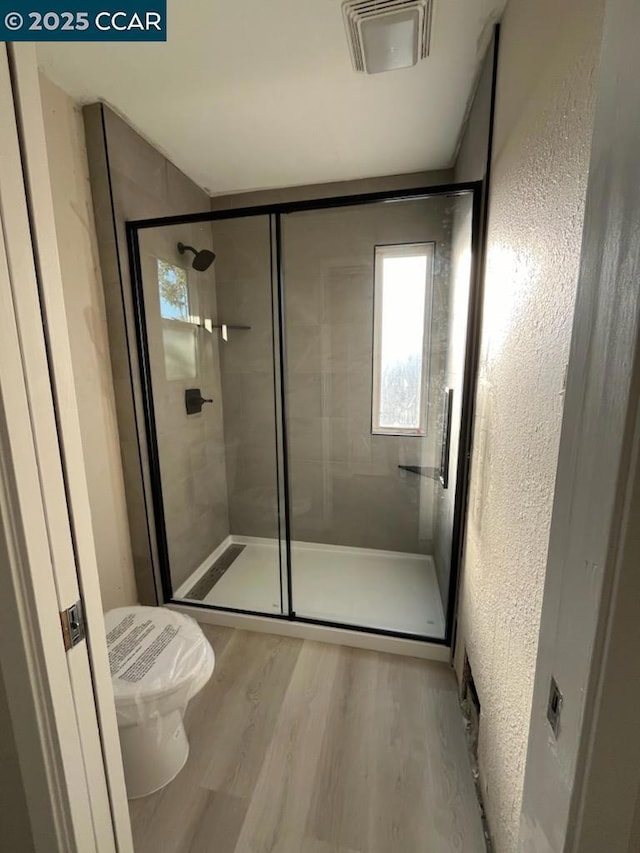 bathroom featuring wood-type flooring, a shower with door, and toilet