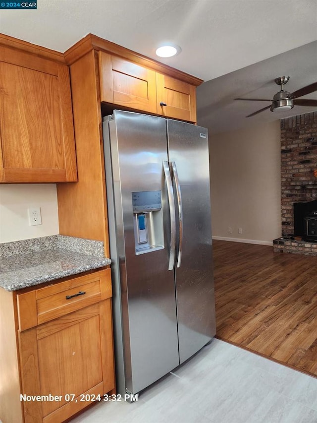 kitchen featuring light hardwood / wood-style flooring, ceiling fan, light stone counters, stainless steel fridge with ice dispenser, and a wood stove