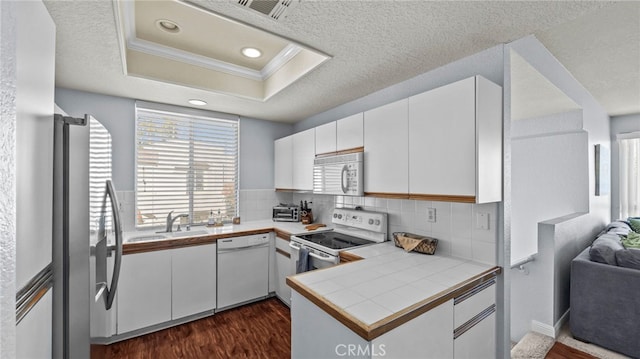 kitchen with kitchen peninsula, white appliances, dark hardwood / wood-style floors, and white cabinetry