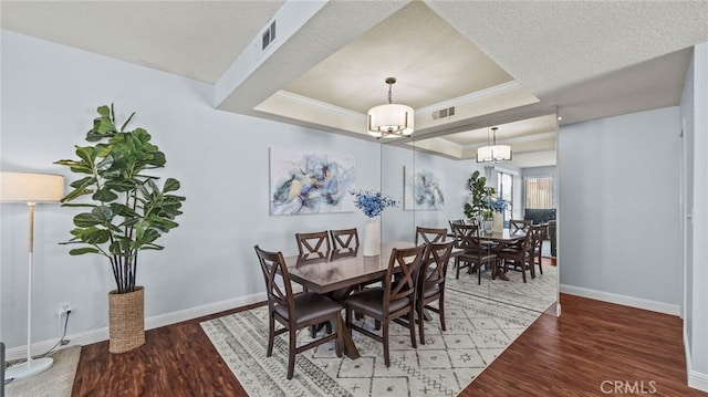 dining room featuring a textured ceiling, dark hardwood / wood-style flooring, an inviting chandelier, and a raised ceiling