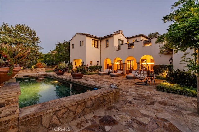 back house at dusk with a patio area and a balcony