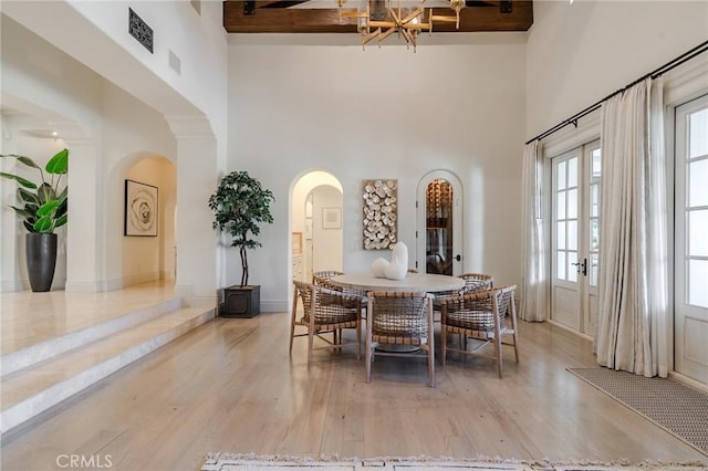 dining room with beamed ceiling, hardwood / wood-style floors, a towering ceiling, and french doors