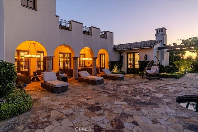 back house at dusk with french doors, a balcony, a patio, and a hot tub