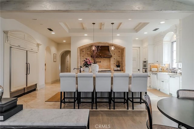 kitchen with decorative light fixtures, a raised ceiling, light wood-type flooring, and a kitchen island with sink