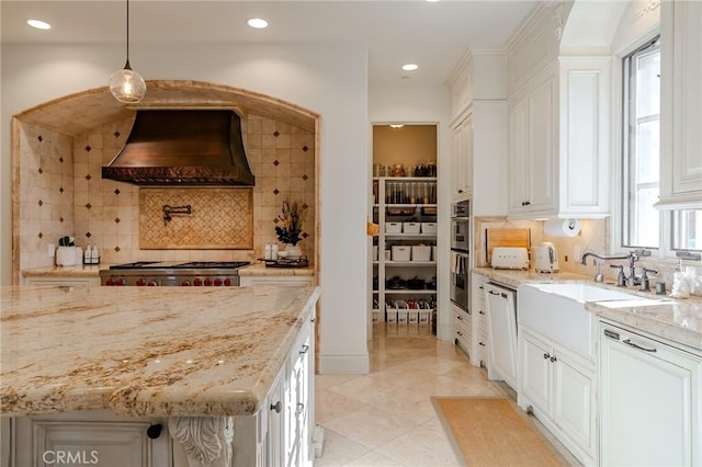 kitchen featuring light stone countertops, decorative light fixtures, premium range hood, and white cabinetry