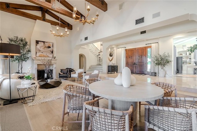 dining area with a chandelier, beam ceiling, high vaulted ceiling, and a fireplace