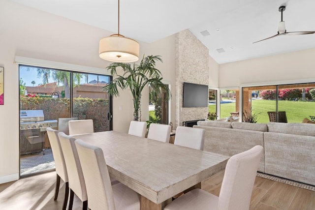 dining space with a fireplace, ceiling fan, light hardwood / wood-style flooring, and high vaulted ceiling