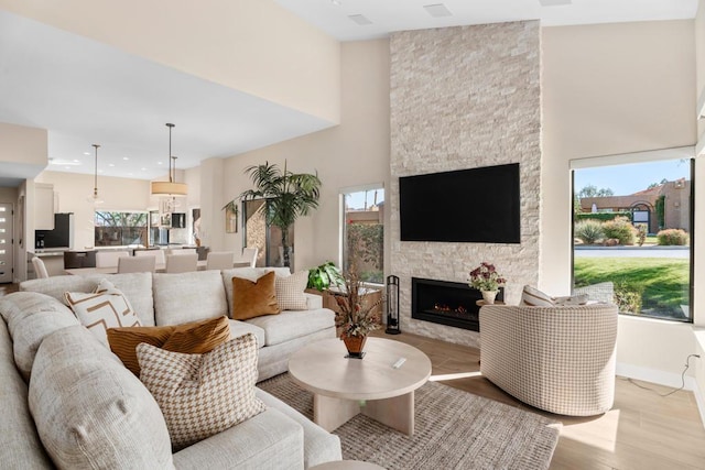 living room featuring a stone fireplace, light wood-type flooring, and a high ceiling