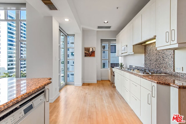 kitchen featuring white appliances, backsplash, light hardwood / wood-style flooring, stone countertops, and white cabinetry