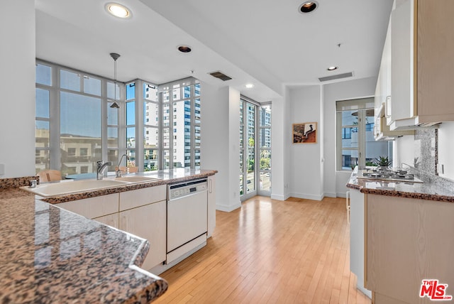 kitchen featuring stainless steel gas stovetop, white dishwasher, sink, light hardwood / wood-style flooring, and stone countertops