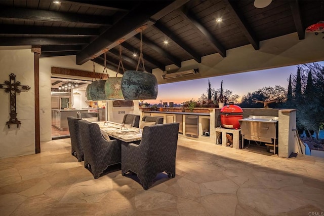 patio terrace at dusk featuring an outdoor kitchen and a grill