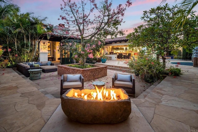 patio terrace at dusk featuring an outdoor living space with a fire pit and area for grilling