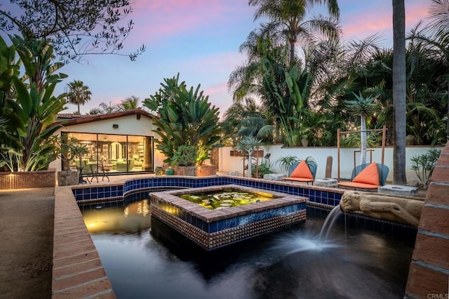 pool at dusk featuring a patio area and a hot tub