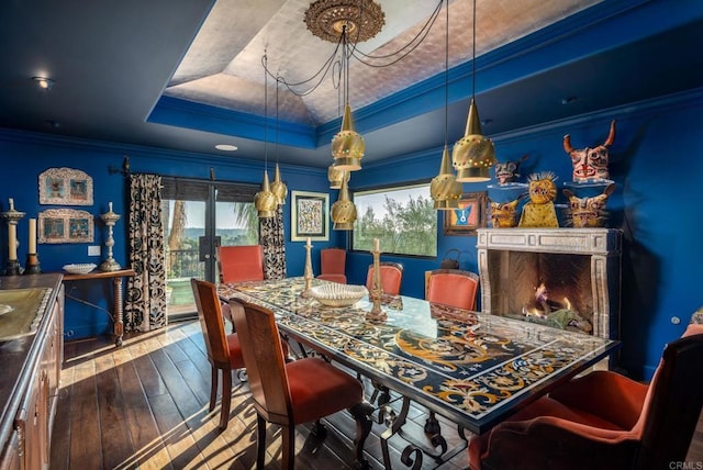 dining area with hardwood / wood-style floors, a premium fireplace, a raised ceiling, and ornamental molding