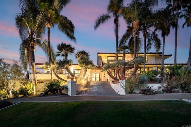 view of front of home with stucco siding, a front lawn, a tile roof, and french doors