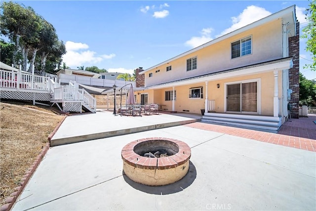 back of house featuring a deck, an outdoor fire pit, and a patio