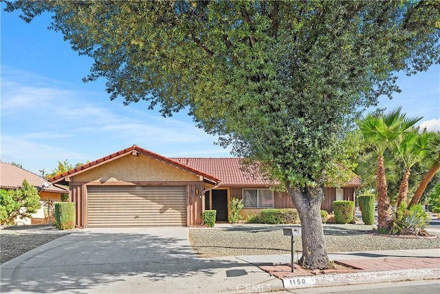 ranch-style home featuring driveway, a tile roof, a garage, and stucco siding