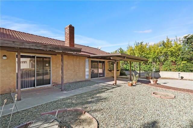back of house featuring a chimney, stucco siding, a tiled roof, and a patio