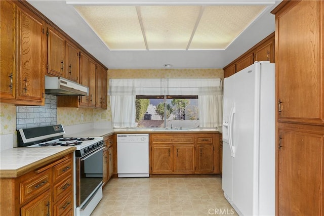 kitchen featuring decorative backsplash, white appliances, brown cabinets, under cabinet range hood, and tile countertops