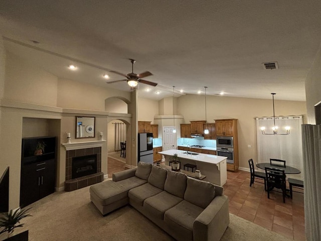 tiled living room featuring a fireplace, ceiling fan with notable chandelier, vaulted ceiling, and sink