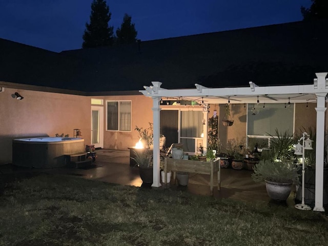 back house at night featuring a patio area, a pergola, and a hot tub