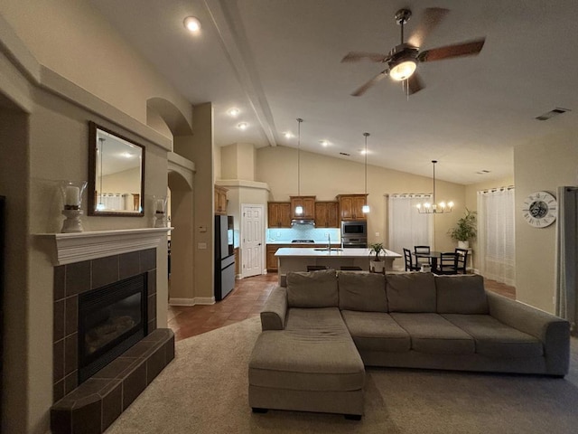 living room with ceiling fan with notable chandelier, a tiled fireplace, sink, and vaulted ceiling