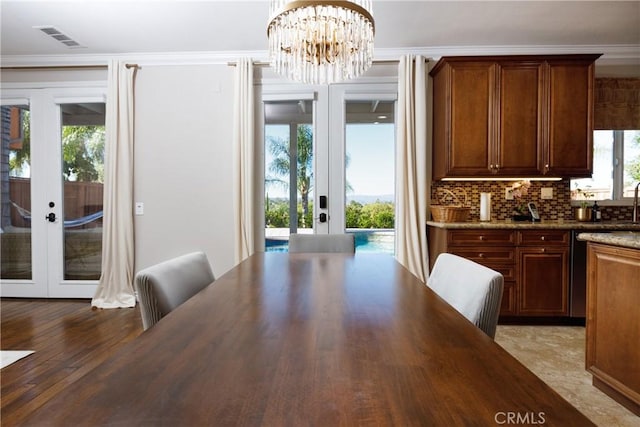 unfurnished dining area with french doors, an inviting chandelier, plenty of natural light, and crown molding