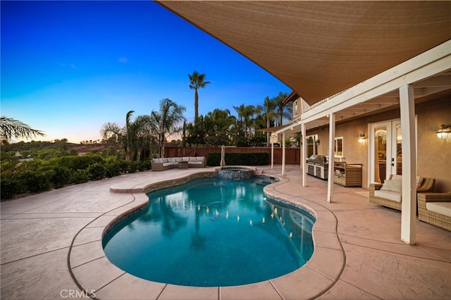 pool at dusk with an outdoor kitchen, an outdoor hangout area, french doors, and a patio