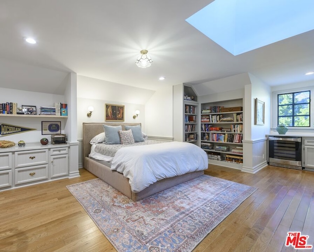 bedroom featuring light wood-type flooring, wine cooler, and vaulted ceiling with skylight