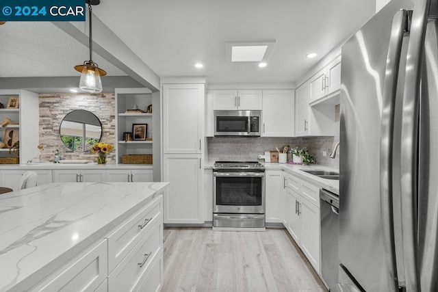 kitchen with sink, appliances with stainless steel finishes, decorative light fixtures, white cabinets, and light wood-type flooring