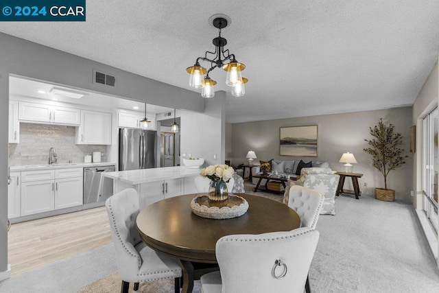 dining area with sink, light wood-type flooring, a textured ceiling, and a chandelier