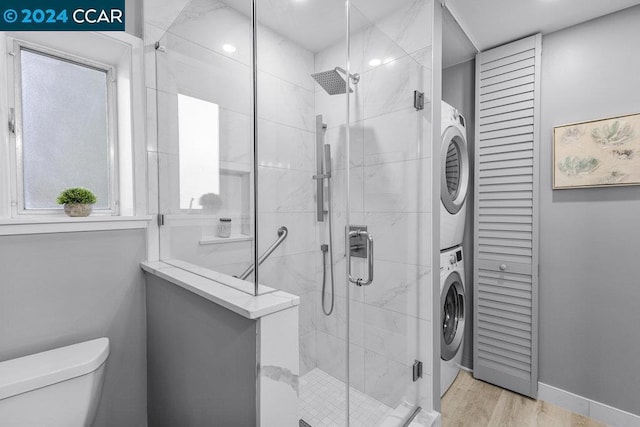 bathroom featuring hardwood / wood-style floors, toilet, stacked washer and dryer, and walk in shower