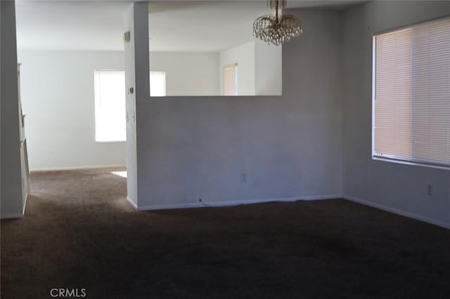 unfurnished room with dark colored carpet and an inviting chandelier