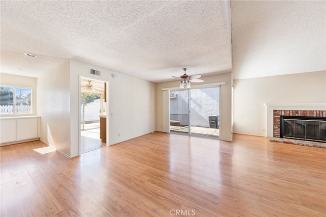 unfurnished living room with a brick fireplace, a textured ceiling, light hardwood / wood-style flooring, and a healthy amount of sunlight