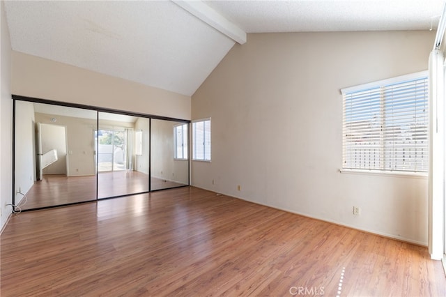 unfurnished bedroom featuring high vaulted ceiling, light wood-type flooring, a textured ceiling, beamed ceiling, and a closet