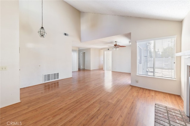 unfurnished living room with ceiling fan, light hardwood / wood-style flooring, high vaulted ceiling, a textured ceiling, and a fireplace