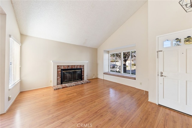 unfurnished living room featuring a textured ceiling, light wood-type flooring, high vaulted ceiling, and a brick fireplace