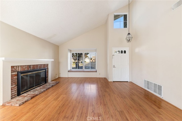 unfurnished living room with wood-type flooring, a textured ceiling, high vaulted ceiling, and a brick fireplace