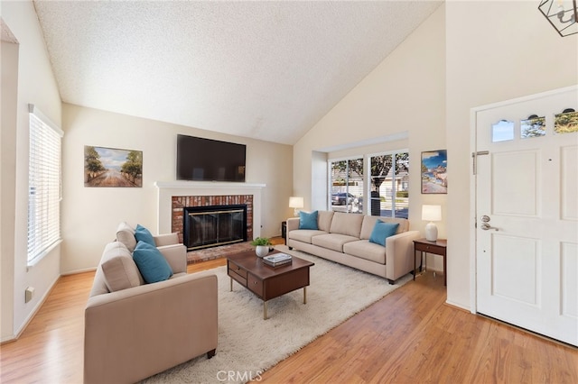 living room featuring light wood-type flooring, a textured ceiling, high vaulted ceiling, and a brick fireplace