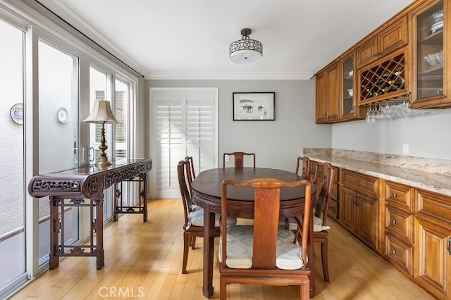 dining space featuring bar area, light hardwood / wood-style floors, and ornamental molding