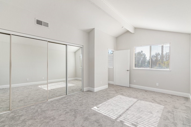 unfurnished bedroom with lofted ceiling with beams, light colored carpet, and a closet