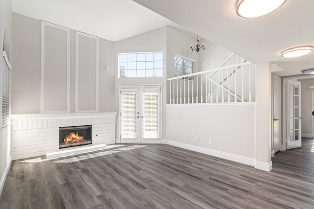 unfurnished living room featuring french doors, dark hardwood / wood-style flooring, an inviting chandelier, and a brick fireplace