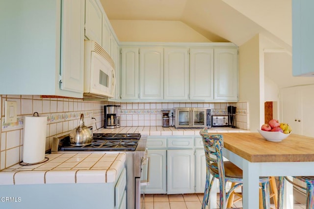 kitchen with light tile patterned flooring, tile countertops, white appliances, and decorative backsplash