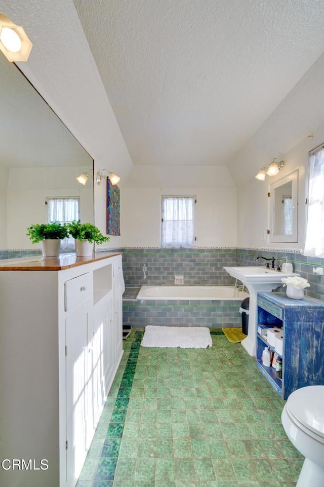 bathroom with sink, tiled bath, a textured ceiling, and tile walls