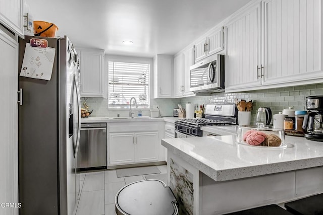 kitchen with sink, tasteful backsplash, kitchen peninsula, white cabinets, and appliances with stainless steel finishes