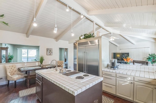 kitchen with ceiling fan, vaulted ceiling with beams, dark hardwood / wood-style flooring, stainless steel built in refrigerator, and tile countertops