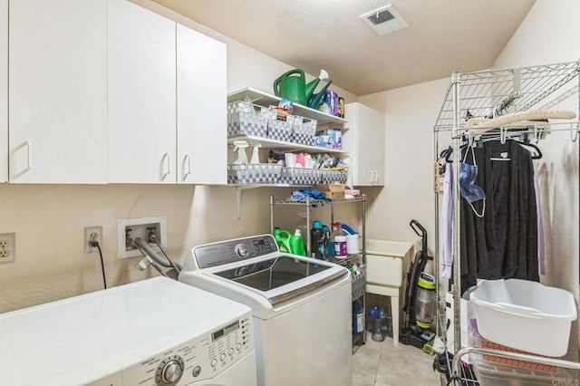 laundry room with washer and clothes dryer, cabinets, light tile patterned floors, and a textured ceiling