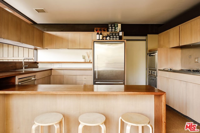 kitchen with wooden counters, sink, appliances with stainless steel finishes, a kitchen bar, and kitchen peninsula