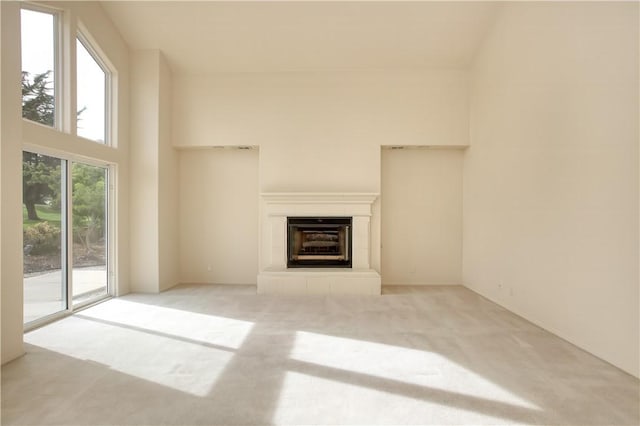 unfurnished living room with a tile fireplace, a towering ceiling, and light colored carpet