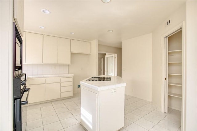 kitchen featuring tile counters, light tile patterned floors, a kitchen island, white cabinets, and black appliances